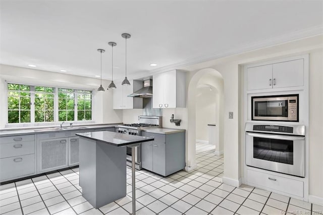 kitchen featuring gray cabinetry, hanging light fixtures, stainless steel appliances, wall chimney exhaust hood, and a center island