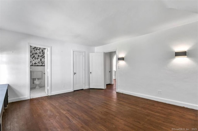 unfurnished bedroom with ensuite bath and dark wood-type flooring