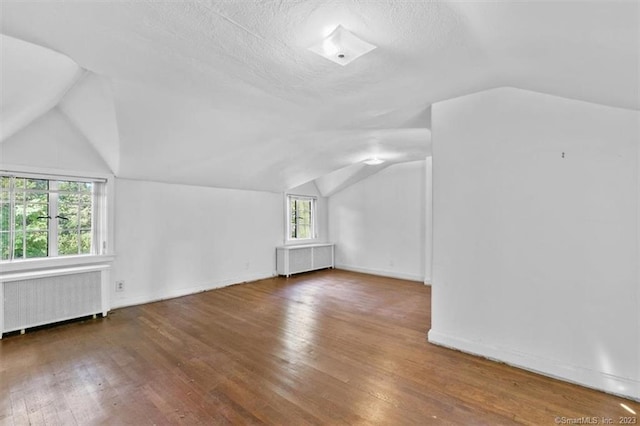 bonus room with dark wood-type flooring, a textured ceiling, radiator heating unit, and vaulted ceiling