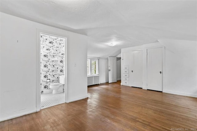 additional living space with dark hardwood / wood-style floors, vaulted ceiling, and radiator heating unit