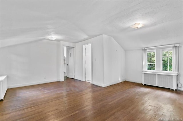 additional living space with dark hardwood / wood-style flooring, lofted ceiling, and radiator