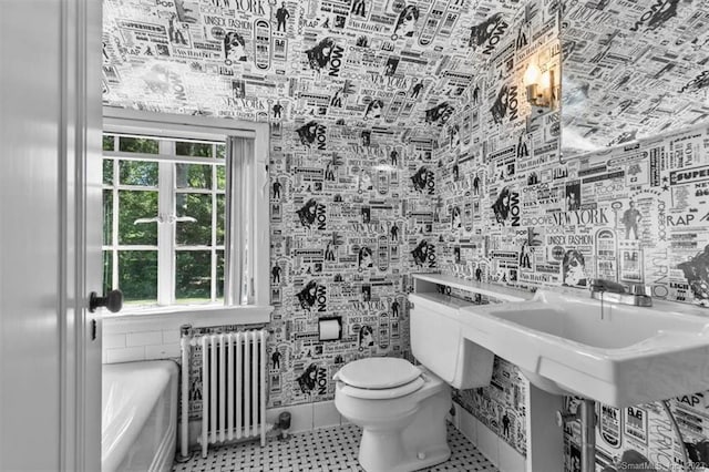 bathroom with toilet, a bathing tub, radiator, tile walls, and tile flooring