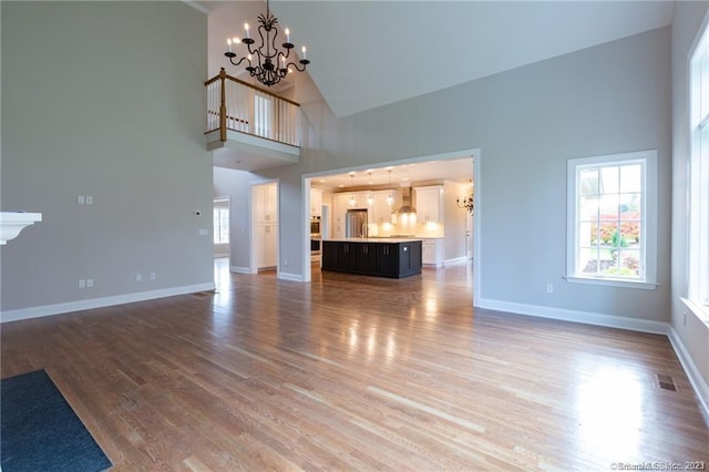 unfurnished living room with an inviting chandelier, high vaulted ceiling, and wood-type flooring