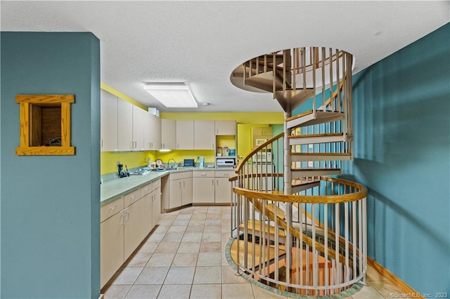 kitchen with light tile flooring, sink, white cabinetry, and a textured ceiling