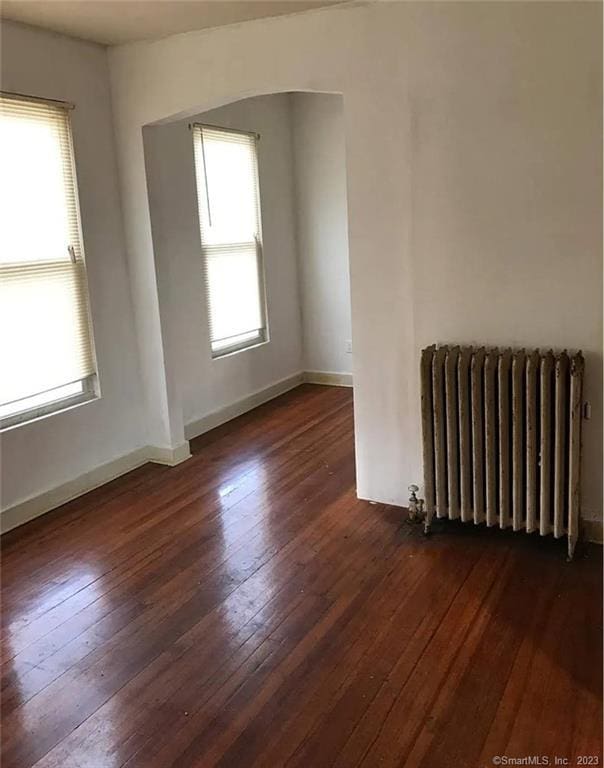 empty room with a healthy amount of sunlight, dark hardwood / wood-style floors, and radiator