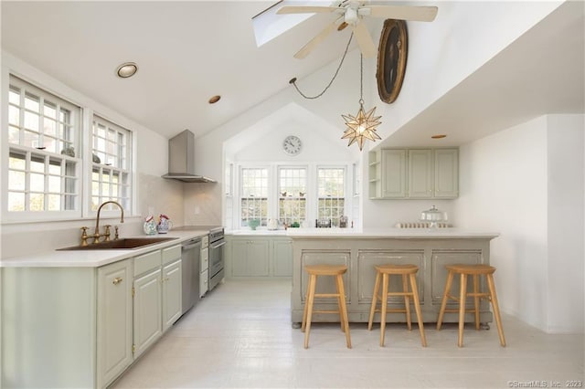 kitchen with stainless steel dishwasher, wall chimney range hood, ceiling fan, vaulted ceiling with skylight, and sink