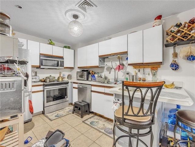 kitchen with white cabinets, a kitchen bar, hanging light fixtures, and appliances with stainless steel finishes