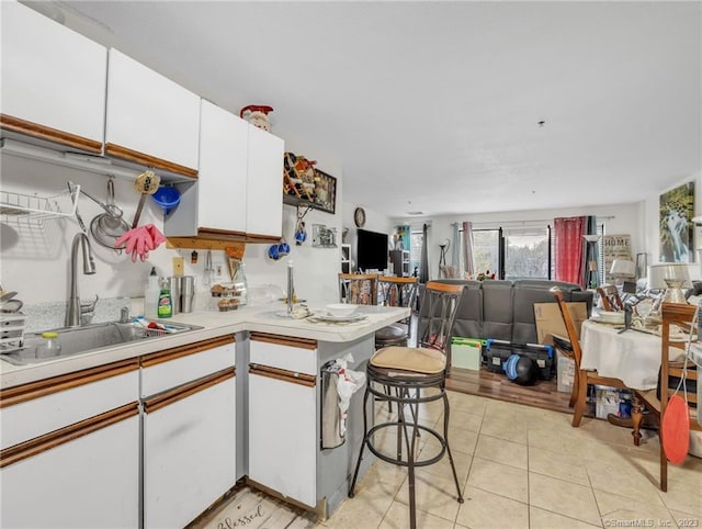 kitchen with kitchen peninsula, sink, light tile floors, white cabinets, and a kitchen bar