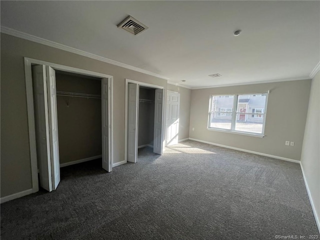 unfurnished bedroom featuring dark carpet, two closets, and ornamental molding