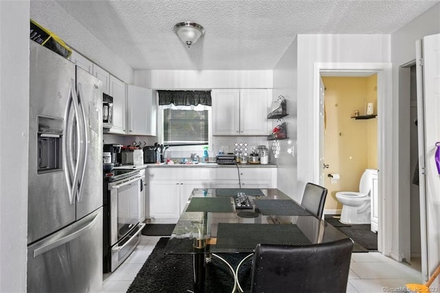 kitchen with white cabinets, a textured ceiling, light tile flooring, and appliances with stainless steel finishes