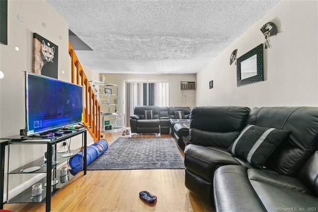 living room with a wall mounted air conditioner, light hardwood / wood-style flooring, and a textured ceiling