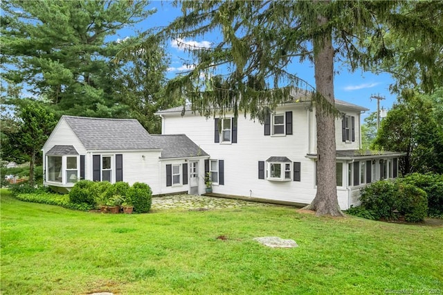 back of house featuring a lawn, a sunroom, and roof with shingles