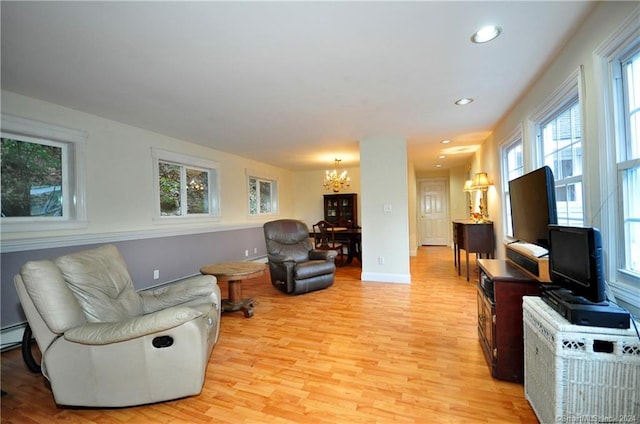 living room featuring light wood-type flooring, baseboard heating, and a notable chandelier