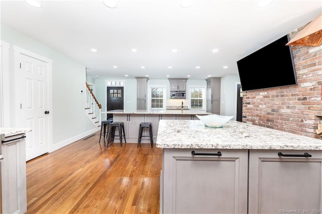 kitchen featuring a kitchen bar, a kitchen island, stainless steel microwave, light hardwood / wood-style floors, and gray cabinetry