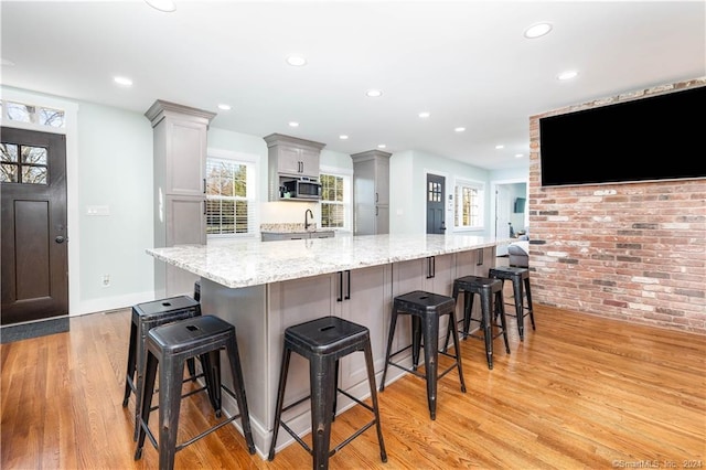 kitchen featuring a breakfast bar, stainless steel microwave, light hardwood / wood-style flooring, and light stone countertops