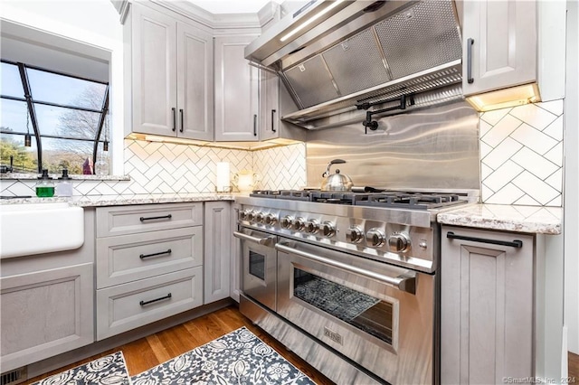 kitchen with light stone countertops, premium range hood, tasteful backsplash, and range with two ovens