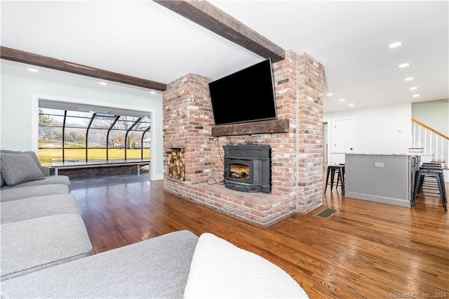 living room with brick wall, a wood stove, and hardwood / wood-style flooring