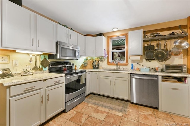 kitchen featuring backsplash, appliances with stainless steel finishes, sink, light tile floors, and white cabinets