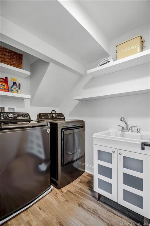 clothes washing area featuring light wood-type flooring, washing machine and clothes dryer, and sink