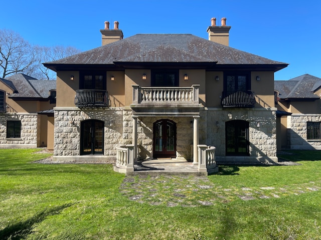 rear view of house with a patio, french doors, a balcony, and a lawn