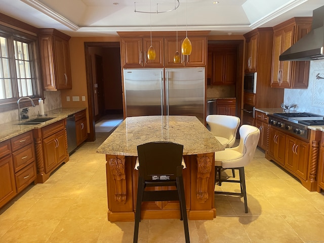 kitchen featuring wall chimney exhaust hood, appliances with stainless steel finishes, a center island, and a raised ceiling