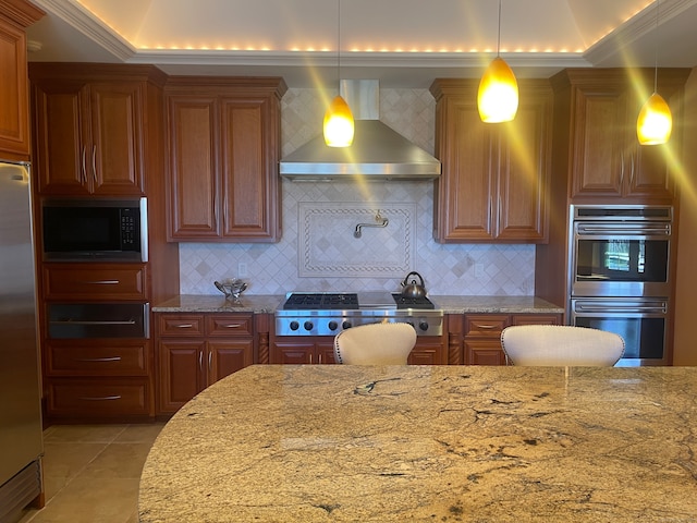 kitchen with light stone counters, appliances with stainless steel finishes, wall chimney exhaust hood, tasteful backsplash, and decorative light fixtures