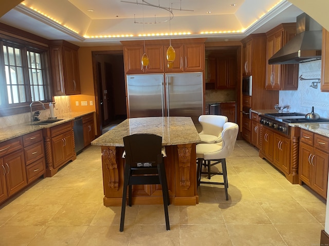 kitchen featuring a raised ceiling, stainless steel appliances, a center island, and wall chimney exhaust hood