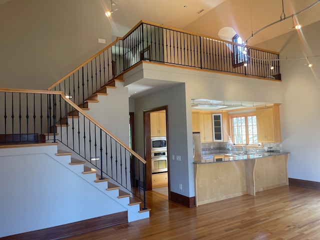 kitchen with high vaulted ceiling, wood-type flooring, tasteful backsplash, and stainless steel appliances