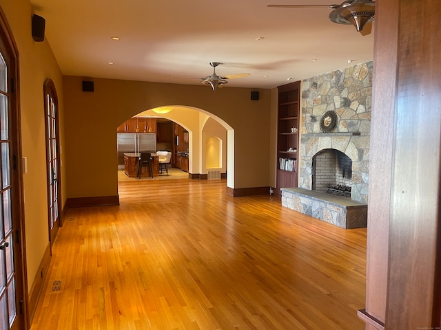 unfurnished living room with hardwood / wood-style flooring, a stone fireplace, built in shelves, and ceiling fan