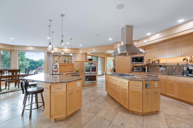 kitchen with decorative light fixtures, appliances with stainless steel finishes, a center island with sink, island range hood, and a breakfast bar area