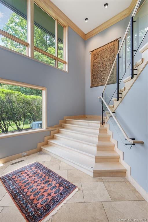 stairs featuring light tile floors, crown molding, and a towering ceiling