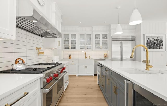 kitchen featuring a sink, white cabinetry, light countertops, wall chimney range hood, and high end appliances