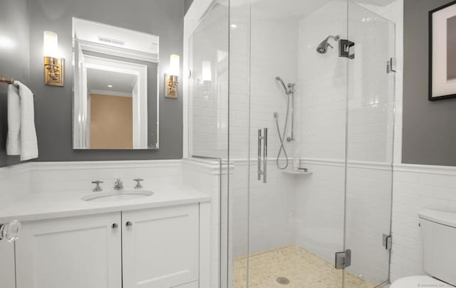 bathroom with toilet, vanity, tile walls, wainscoting, and a shower stall