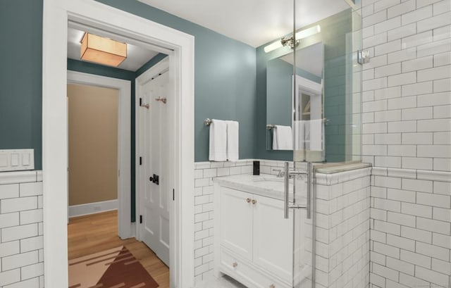 full bath with tile walls, wainscoting, a shower stall, and wood finished floors