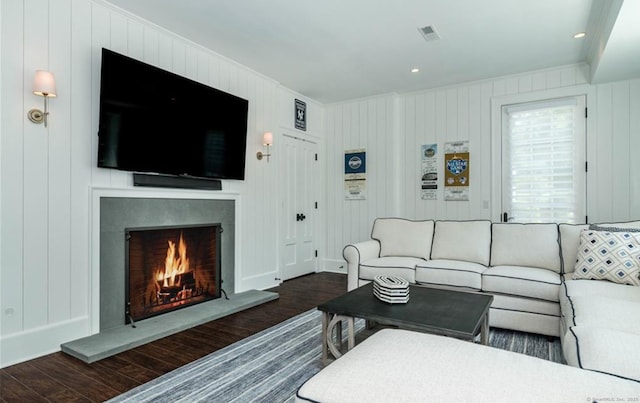 living area with a warm lit fireplace, dark wood-style flooring, and visible vents