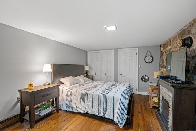 bedroom featuring baseboard heating, dark wood-type flooring, and two closets