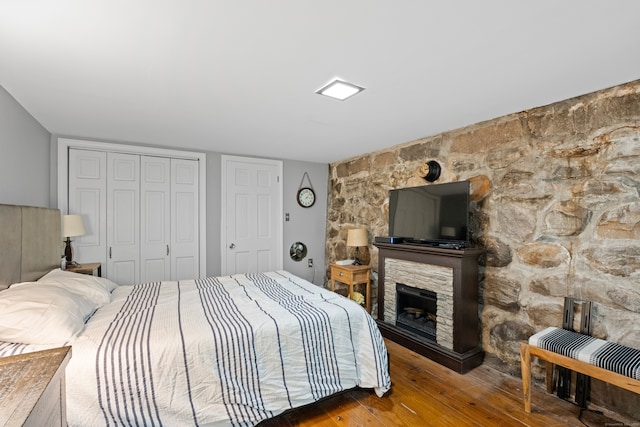 bedroom with a stone fireplace and wood-type flooring