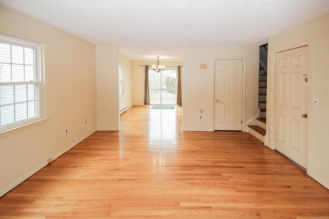 spare room with a chandelier, a textured ceiling, a baseboard heating unit, stairway, and light wood-type flooring