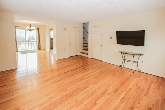 unfurnished living room with a chandelier, a textured ceiling, light wood finished floors, and stairs