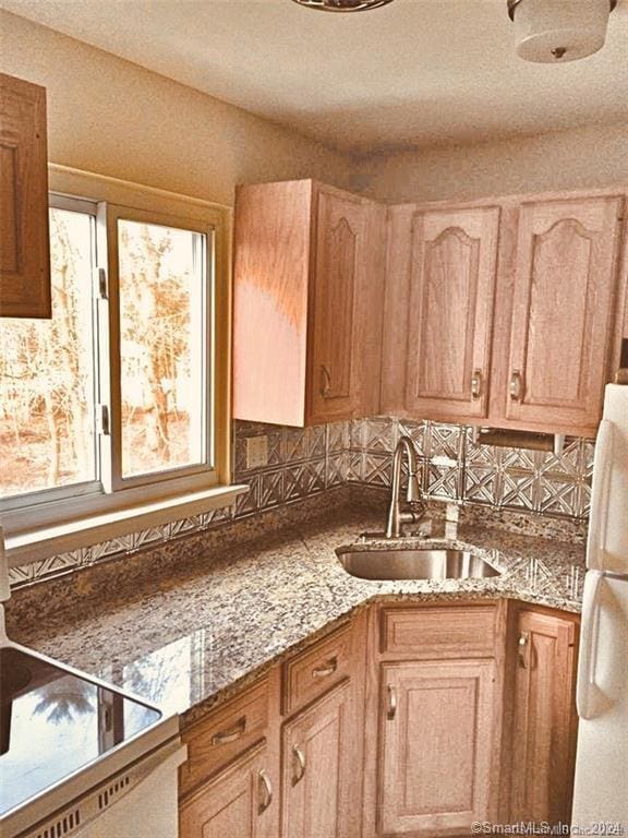 kitchen with white refrigerator, backsplash, light stone counters, and sink