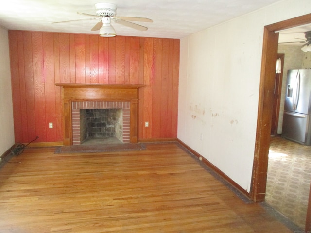 unfurnished living room with wooden walls, light hardwood / wood-style floors, ceiling fan, and a fireplace