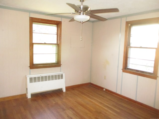 spare room featuring ceiling fan, radiator, hardwood / wood-style floors, and a wealth of natural light