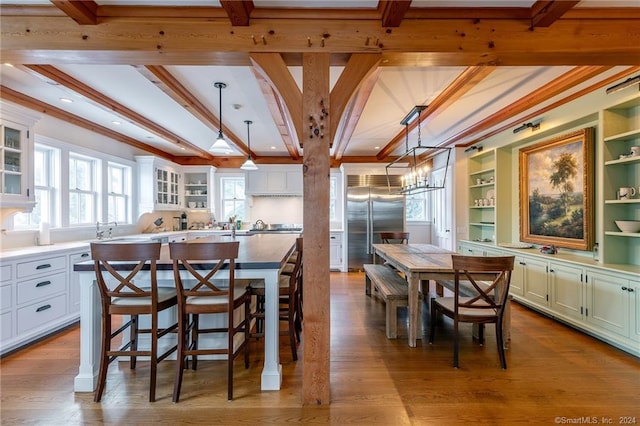 dining area featuring light wood-type flooring, built in shelves, beam ceiling, and ornamental molding