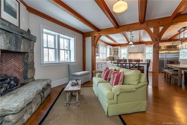 living room with dark wood-type flooring, plenty of natural light, an inviting chandelier, and a stone fireplace