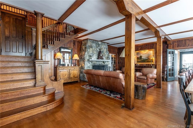 living room featuring a fireplace, wood walls, decorative columns, lofted ceiling with beams, and hardwood / wood-style flooring