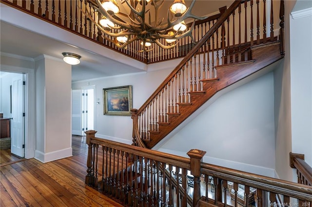 staircase featuring wood-type flooring, a chandelier, and ornamental molding