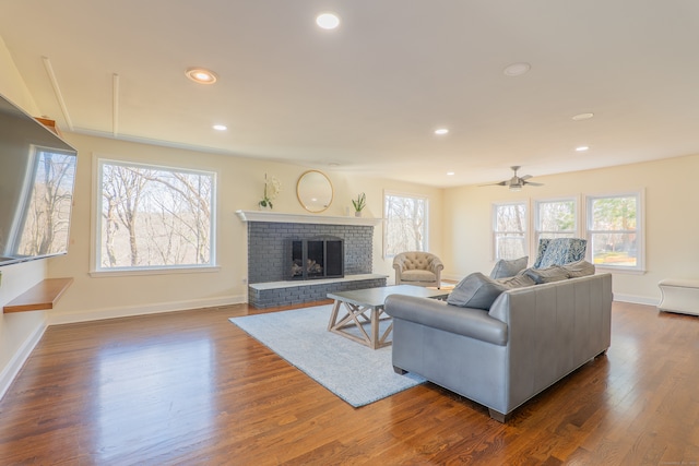 living room with ceiling fan, a healthy amount of sunlight, dark hardwood / wood-style flooring, and a fireplace