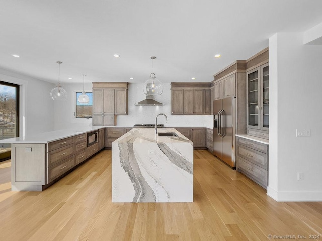 kitchen with decorative light fixtures, a large island with sink, stainless steel appliances, and light wood-type flooring