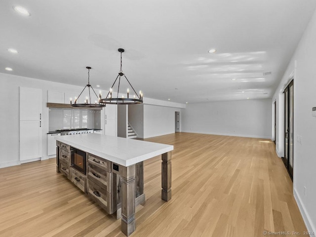 kitchen with hanging light fixtures, black microwave, a center island, and light hardwood / wood-style flooring