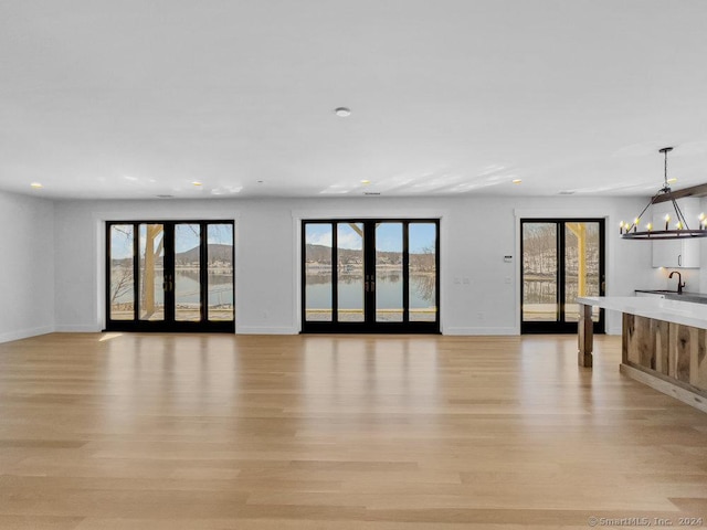 unfurnished living room featuring french doors, sink, a chandelier, and light hardwood / wood-style floors